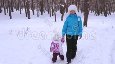在寒冷的冬日，妈妈和小宝宝在针叶林公园里沿着下雪的冬天的散步。 一家人带着小孩散步